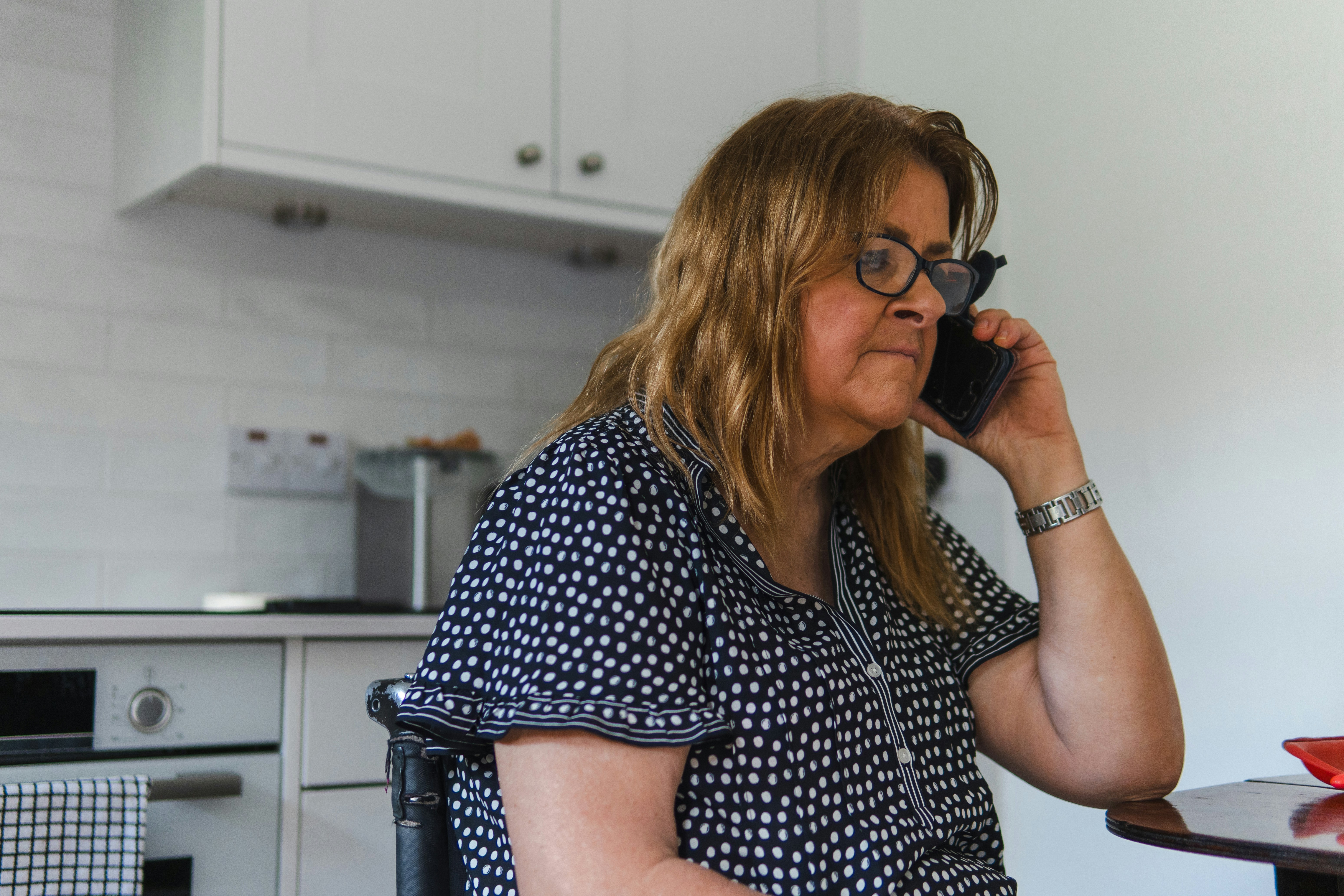 Older woman on a mobile phone in her kitchen, representing the hidden cost of communication-based micro-volunteering